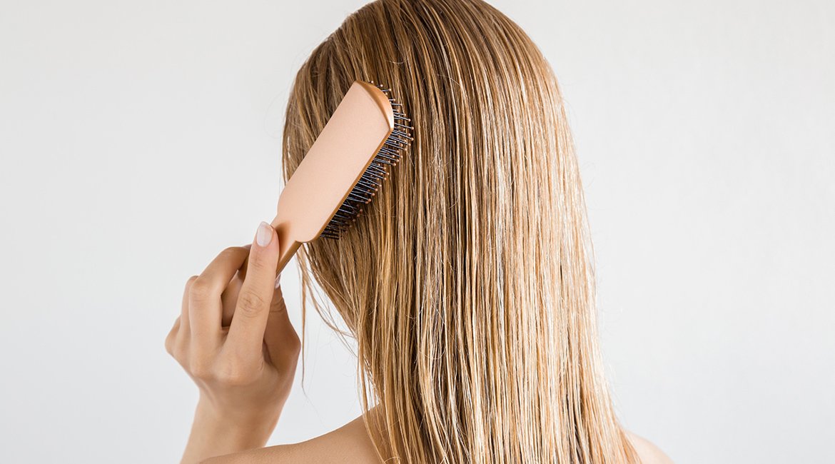 Frau kämmt sich die langen feuchten Haaren mit einer Haarbürste